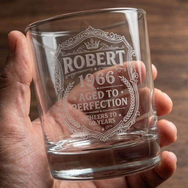 Clear personalized 60th Birthday Gift whiskey glass engraved with name 1966 and aged to perfection crest on a wooden table.