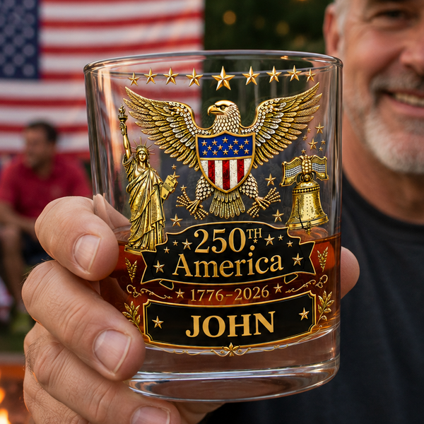 Man holding a personalized glass with an eagle design and '250th America' text, outdoors with a flag in the background.
